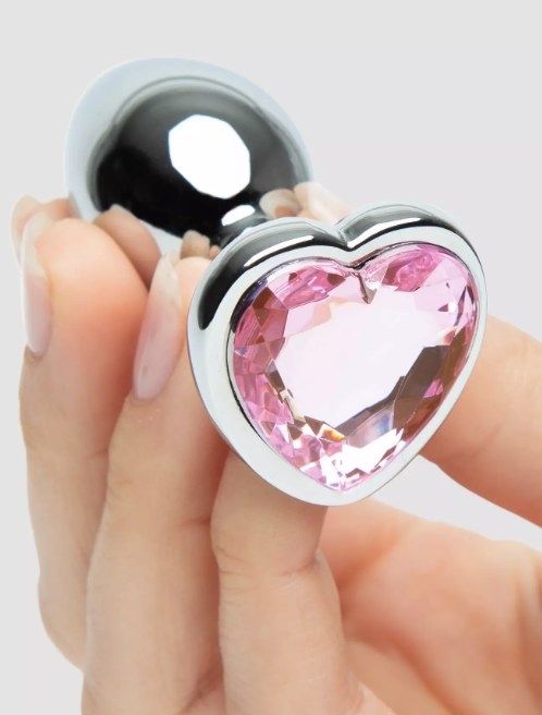 A model holding a pink jeweled heart shaped metal butt plug