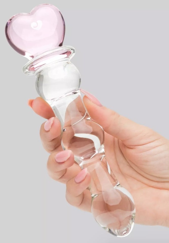 A model holding a wavy glass dildo with a pink heart handle