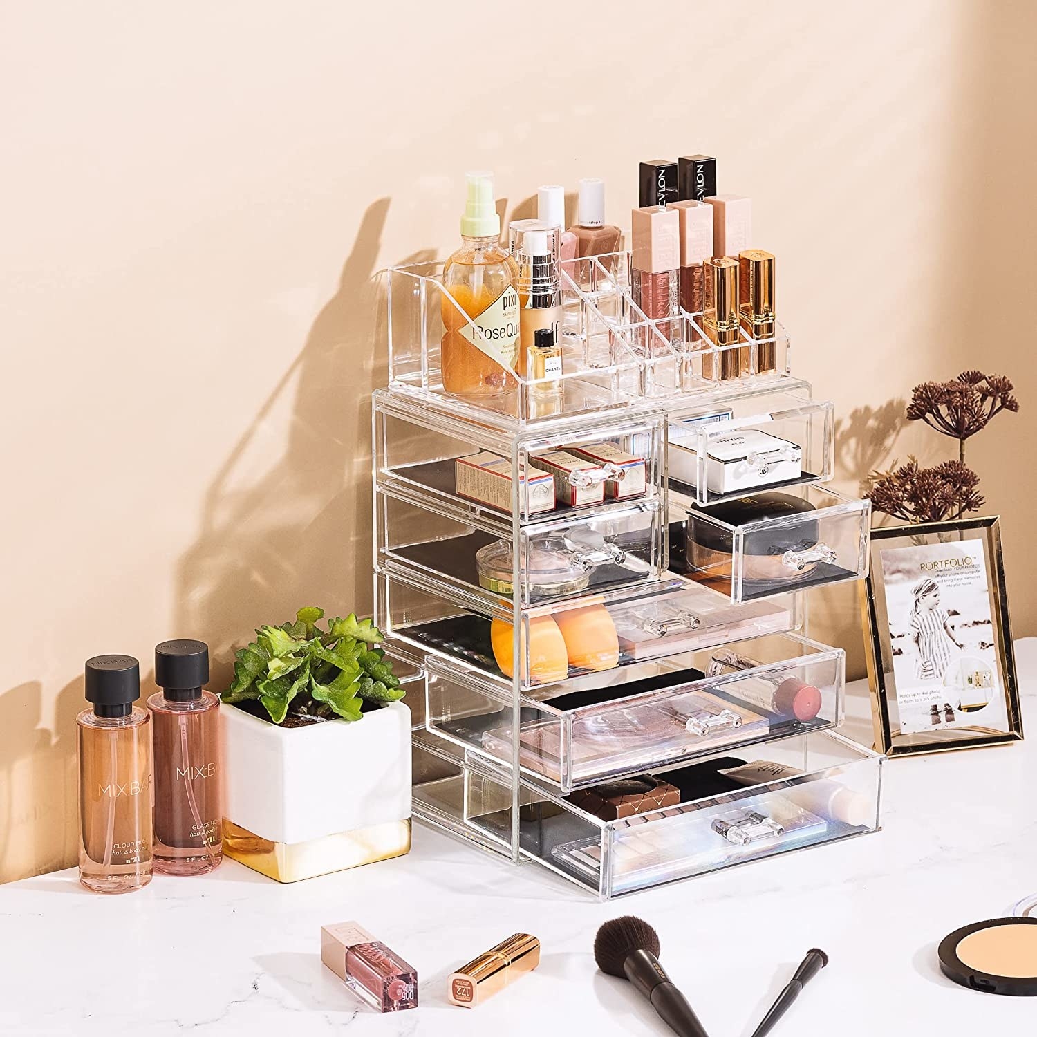 The organizer on a counter holding lipsticks, brushes, lashes, and other makeup in three large drawers, four small drawers,  and extra standing organizers on top