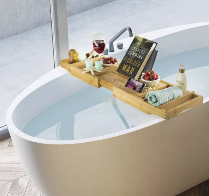 The bath caddy holding a book, phone, wineglass, towel, and candles over a tub