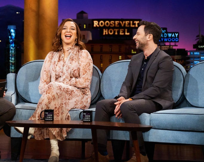 Maya Rudolph sitting on the left next to Nick Kroll on a late-night TV talk show