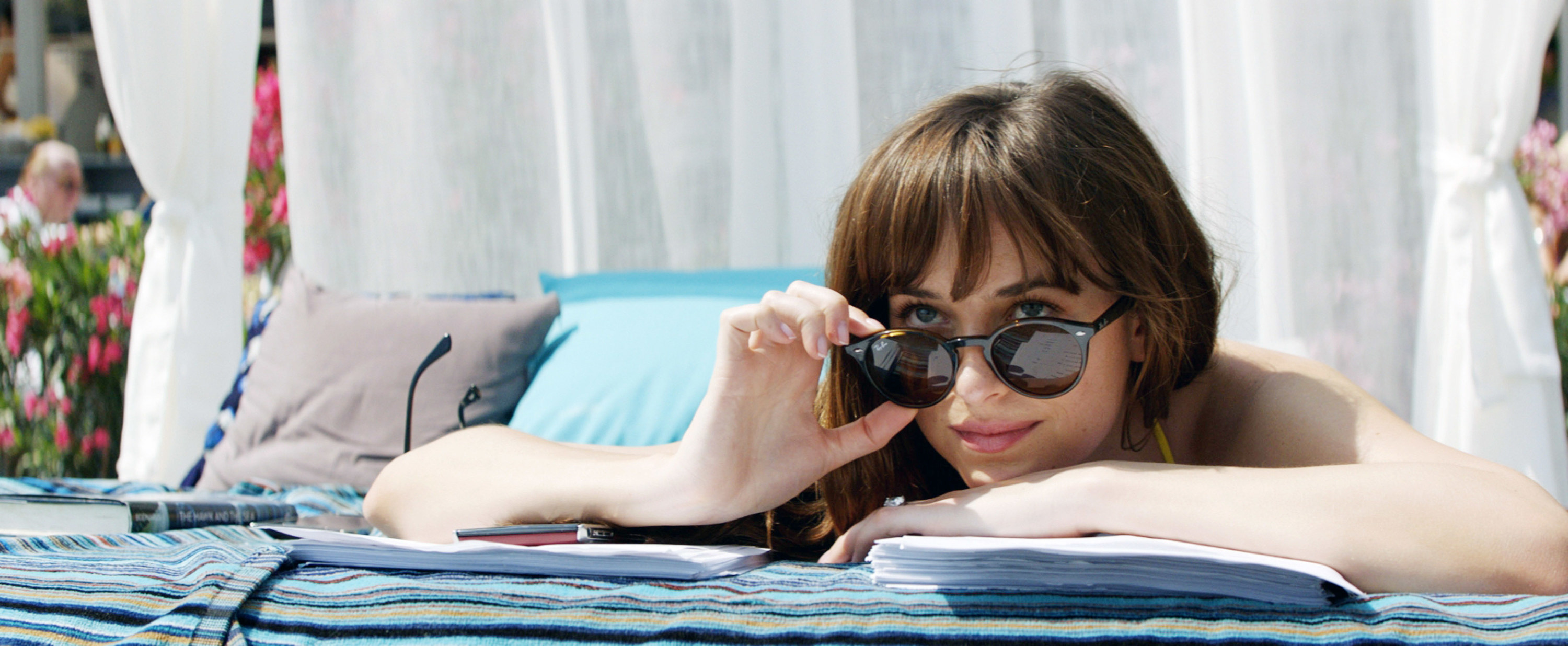 Dakota looks over her sunglasses at something as she lays on her stomach as she lounges by the pool