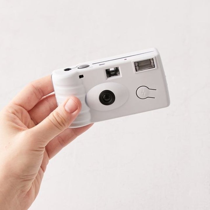a hand holding a small white disposable camera
