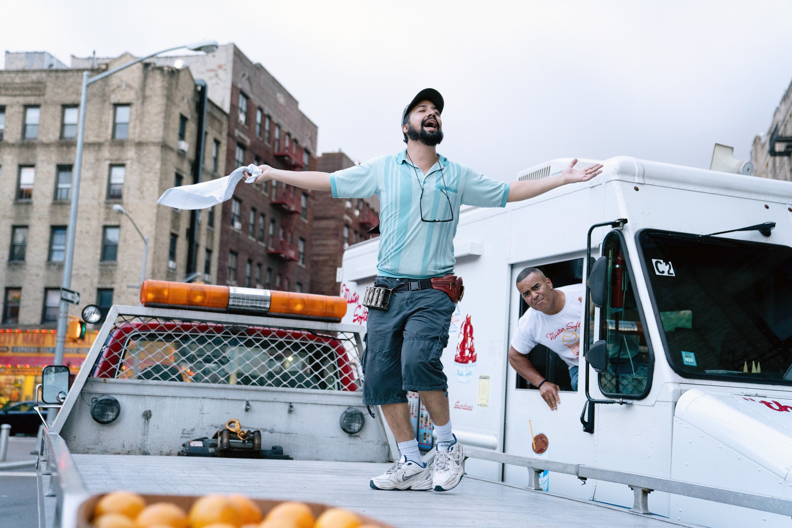 The piragüero dancing on the back of a truck while the Mr. Softee driver watches