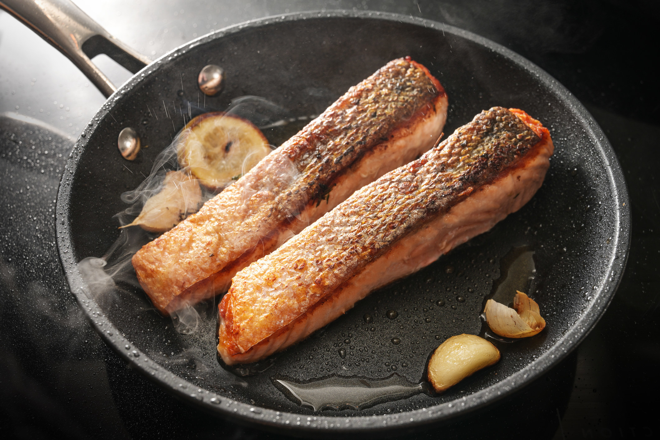 Two pieces of crispy skinned salmon in a pan.