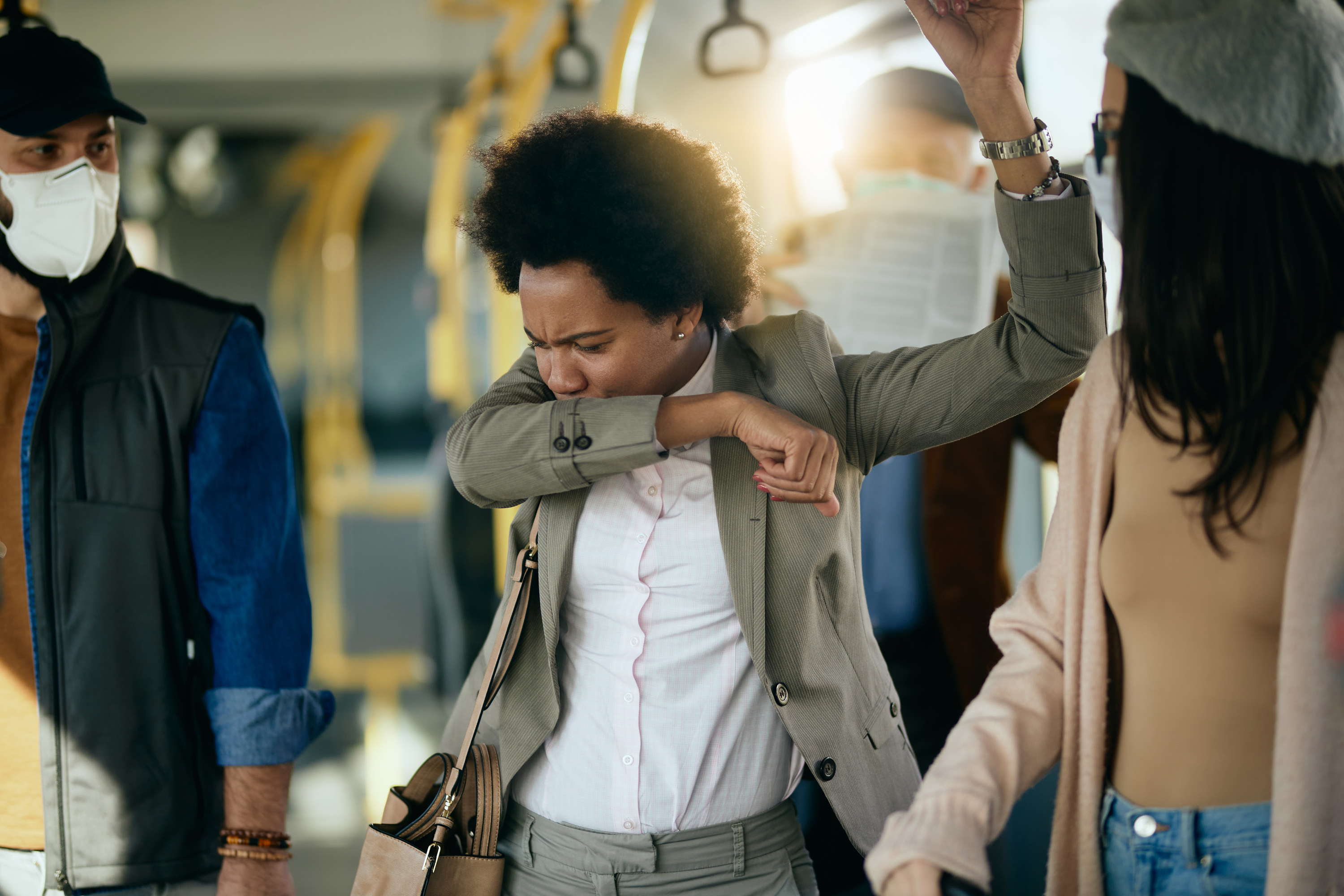 A woman sneezing into her arm while standing on a train with people