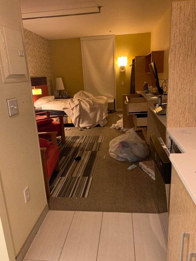 The hotel room as a messily unmade bed, trash and other items on the floor, and all the drawers open