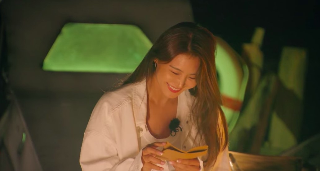 So-yeon smiles down at a postcard