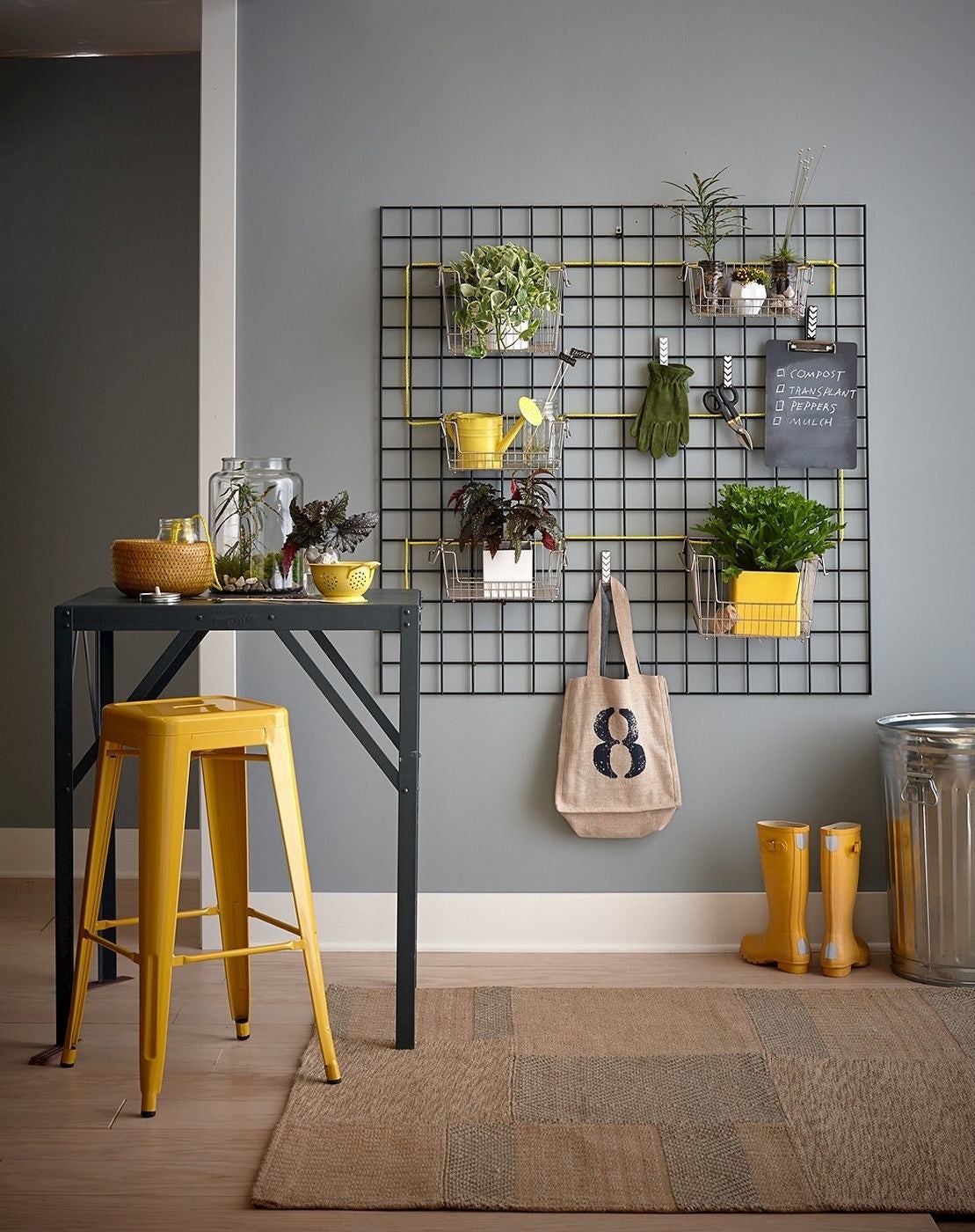 yellow metal stool next to a tall table in a workspace with plants on the wall