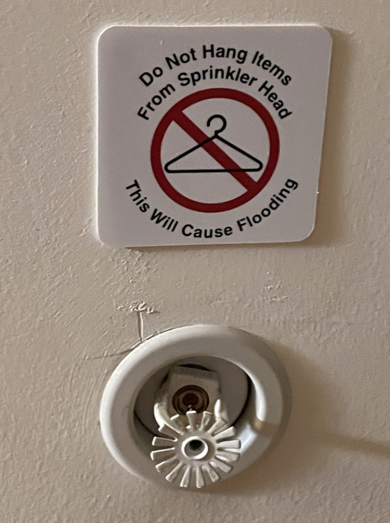 A sprinkler with a sign that says: &quot;Do not hang items from sprinkler head; this will cause flooding&quot;