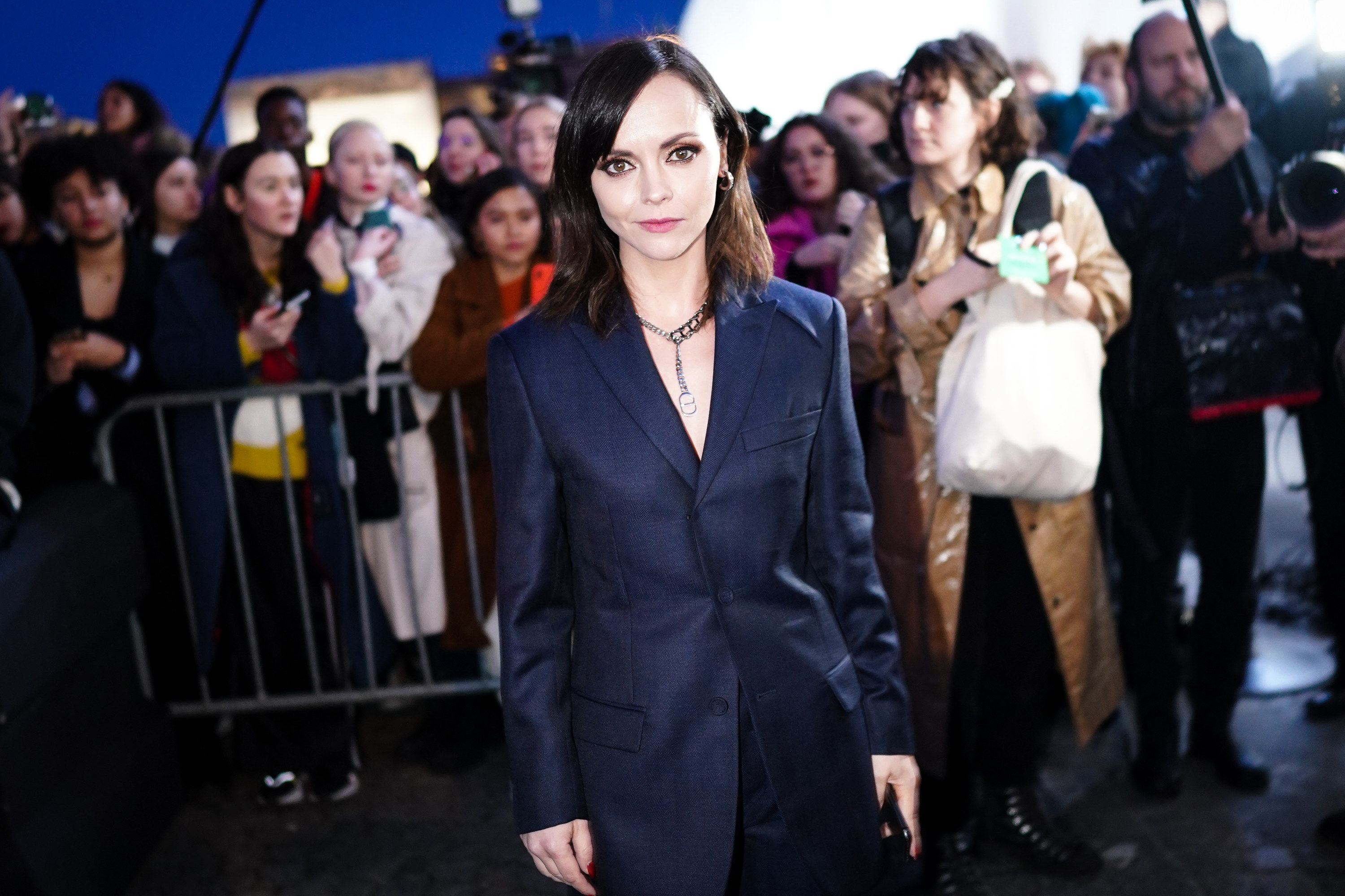 Christina wearing a pantsuit at an event as fans stand behind a barricade behind her