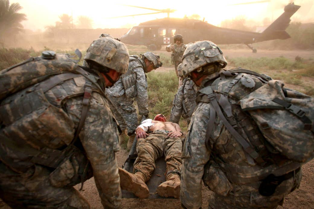 four soldiers carry a wounded soldier to a helicopter