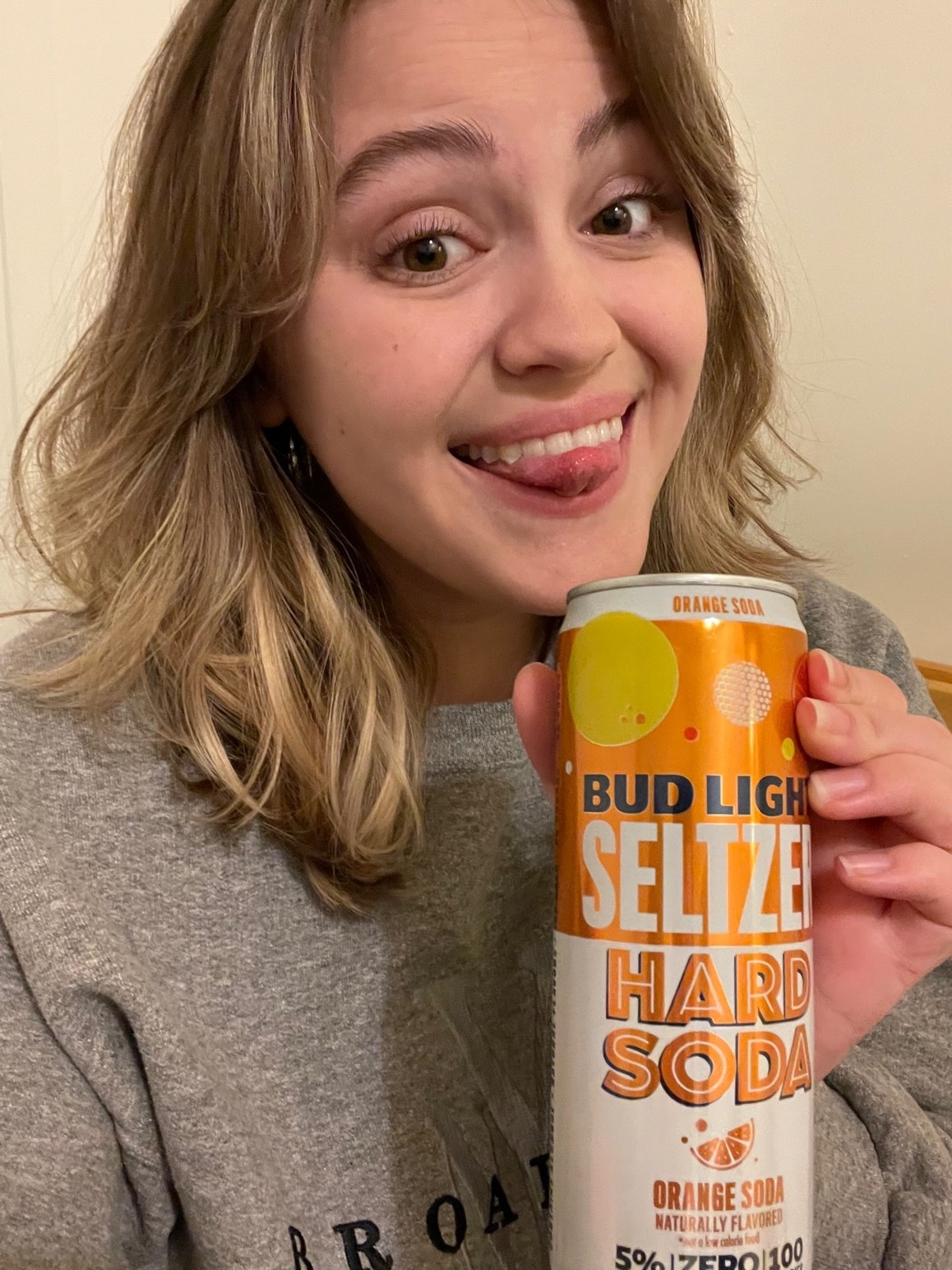 woman smiling giddily with an orange soda hard seltzer