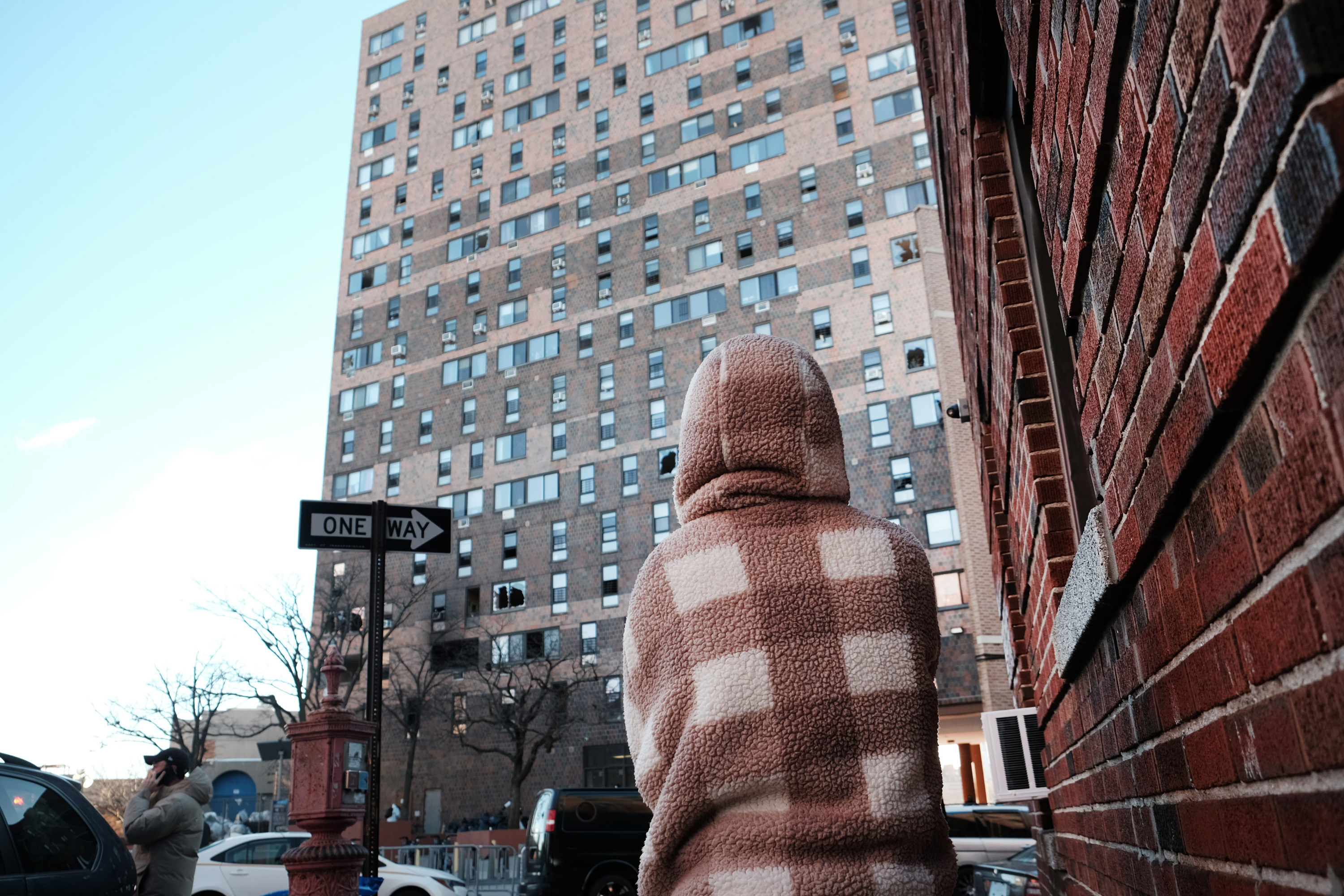 a woman in a fleece hoodie looks at the burned building in a bronx, a one way sign in the background 
