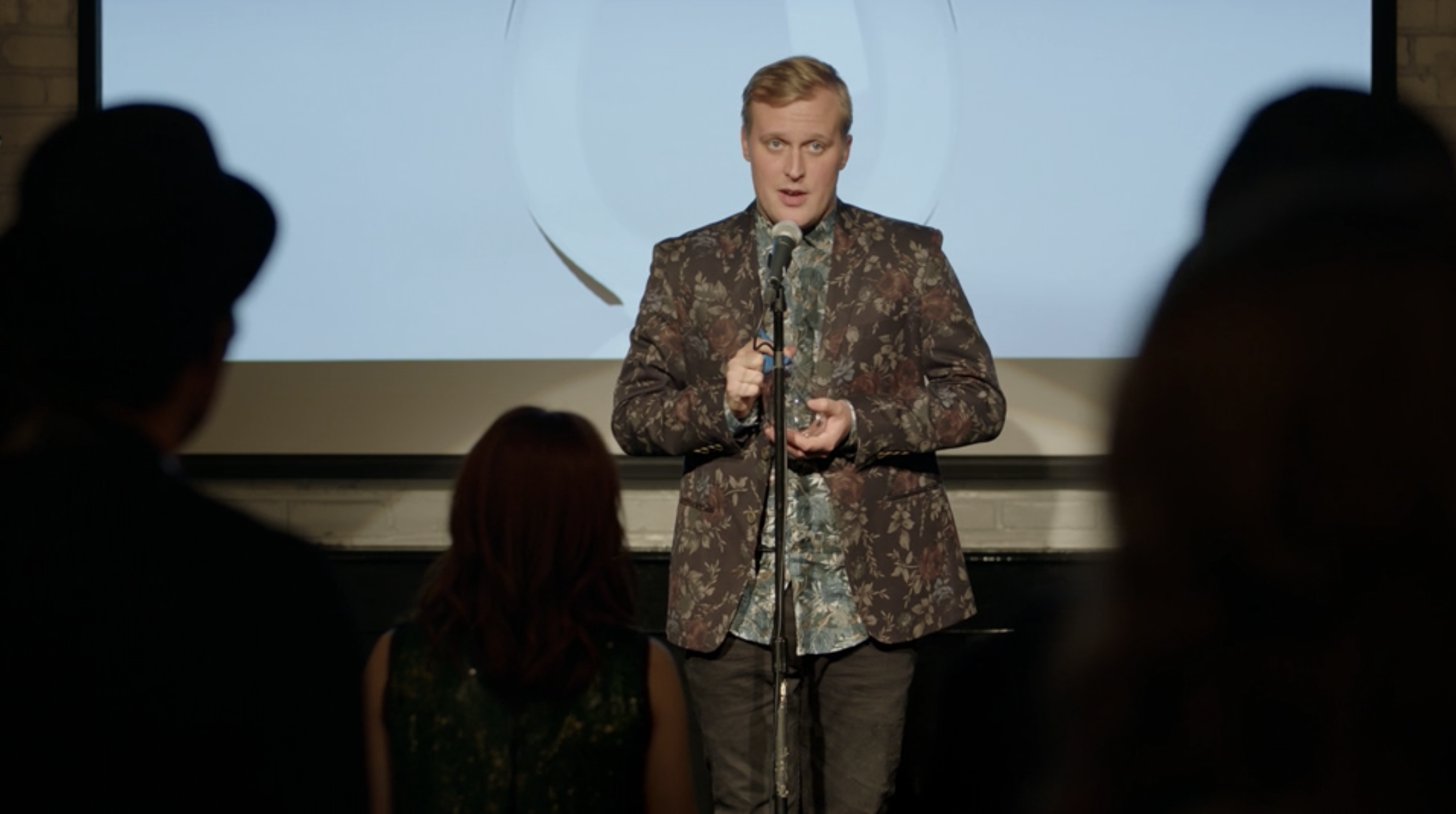 John Early speaking into a microphone.