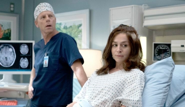 A still from Grey&#x27;s Anatomy showing Amelia in a hospital bed, Dr Koracick standing behind her with scans of her brain on a computer