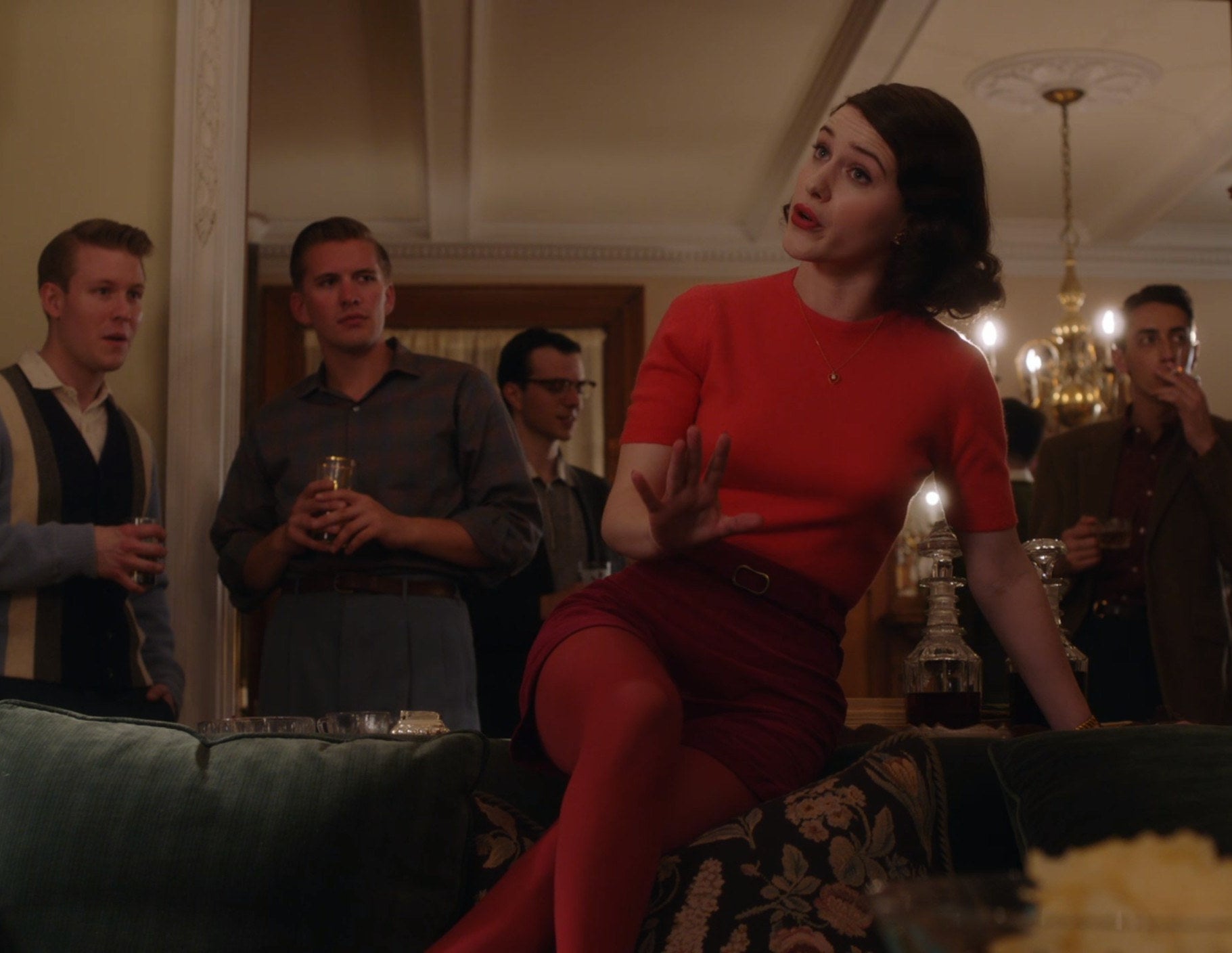 Screenshot from Mrs. Maisel shows Midge in a red outfit sitting on a couch