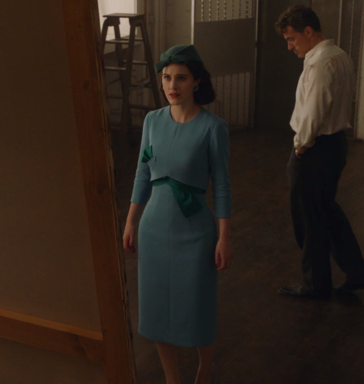 Midge in a fitted below-the-knee dress and green hat