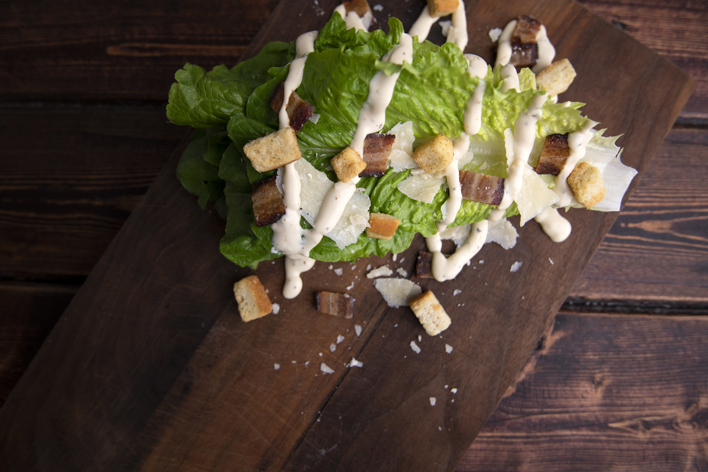 Salad leaves on a wooden cutting board sprinkled with croutons and drizzled with dressing