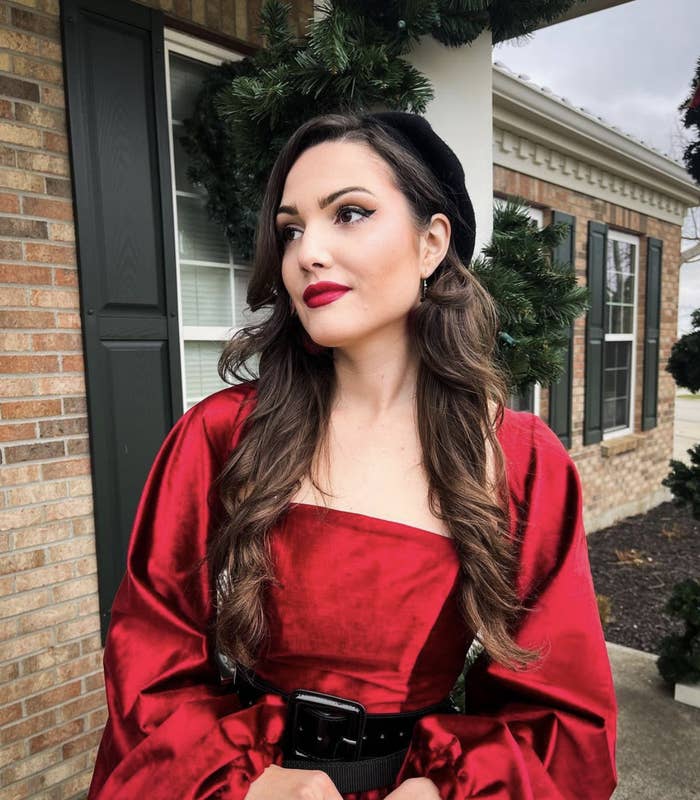 Bonnie wearing a beret and a bright belted dress as she stands outside of a house