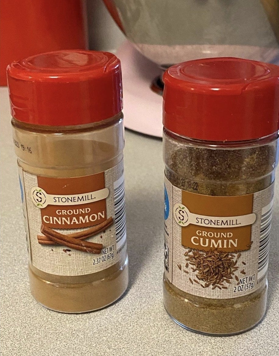 Containers of ground cinnamon and ground cumin side by side