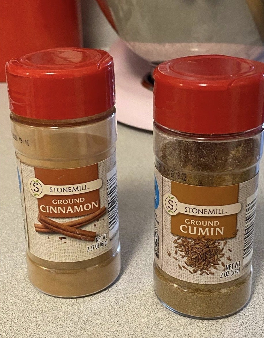Containers of ground cinnamon and ground cumin side by side