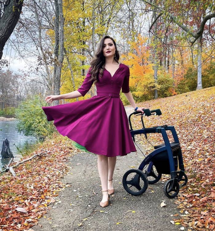 Bonnie posing for a photo on a walking path in the words while wearing a tea-length dress and standing next to her motorized walker
