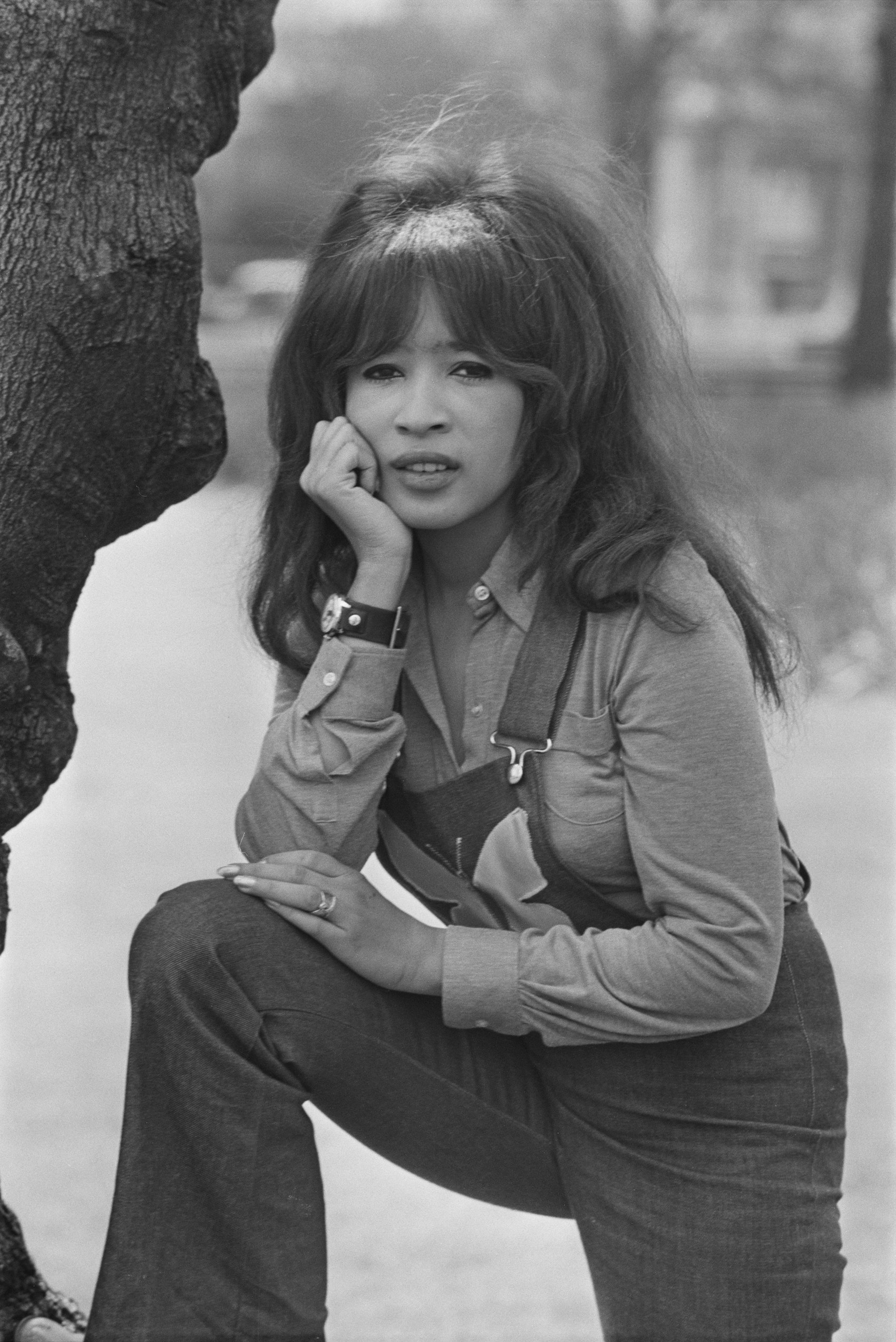 Spector leans against a tree with her hand on her chin