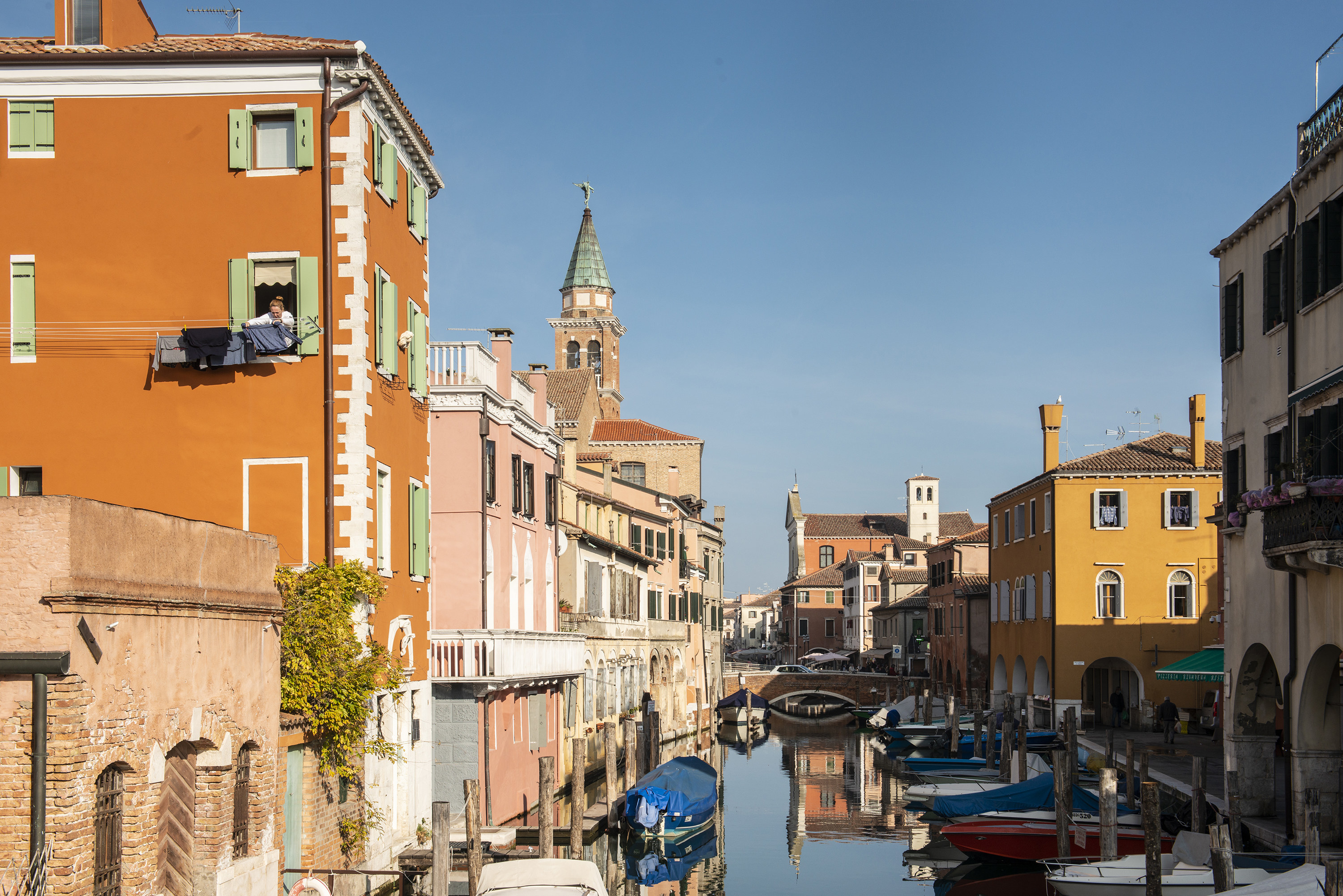 Scene along the Canal Vena, Chioggia, Italy, with a canal and boats and a blue sky