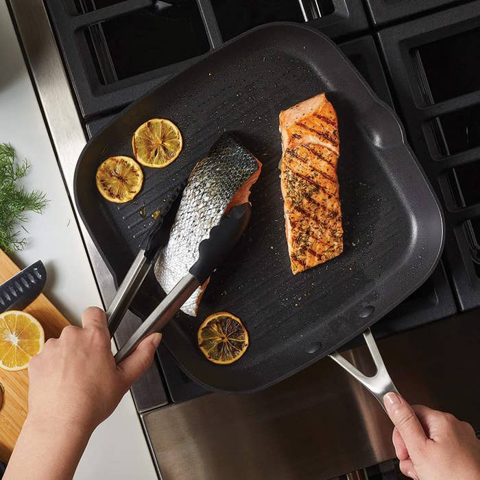A person cooking salmon in the pan
