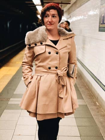a reviewer in a short trench coat with a faux fur hood and a tied belt