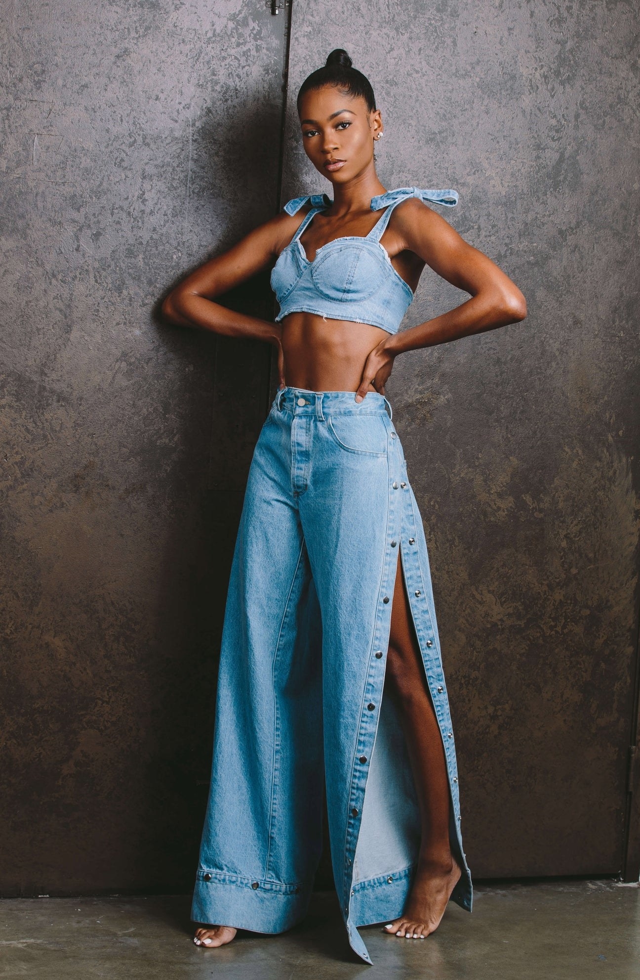 Model wearing wide-leg jeans with button snaps along the side undone and matching denim crop top