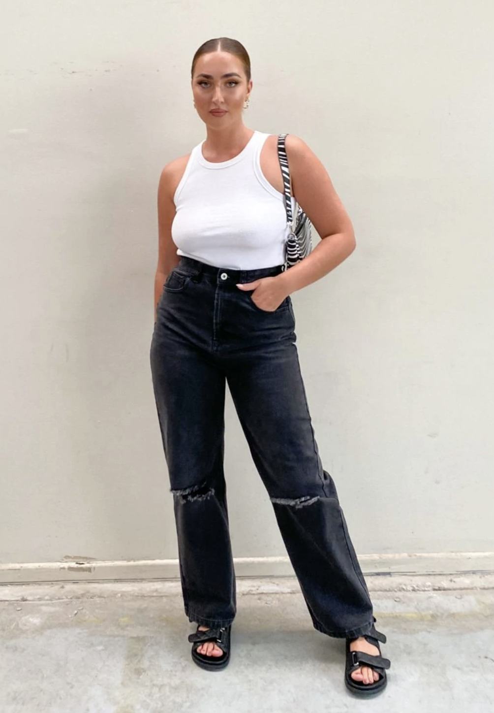 Model wearing black wide-leg jeans with ripped knees and white tank top