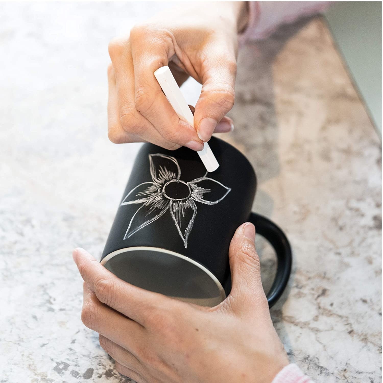 Person drawing a flower on the chalkboard mug