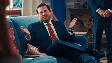 Jonah Hill winking while sitting on a couch in a suit