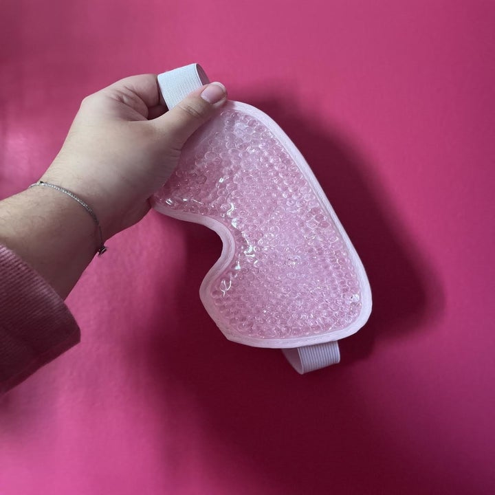 A person holding up the eye mask in front of a wall