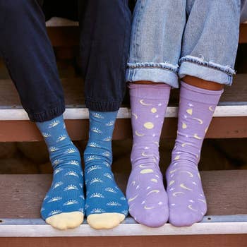 one model wearing a pair of blue socks printed with suns, and a model wearing lilac socks printed with moons