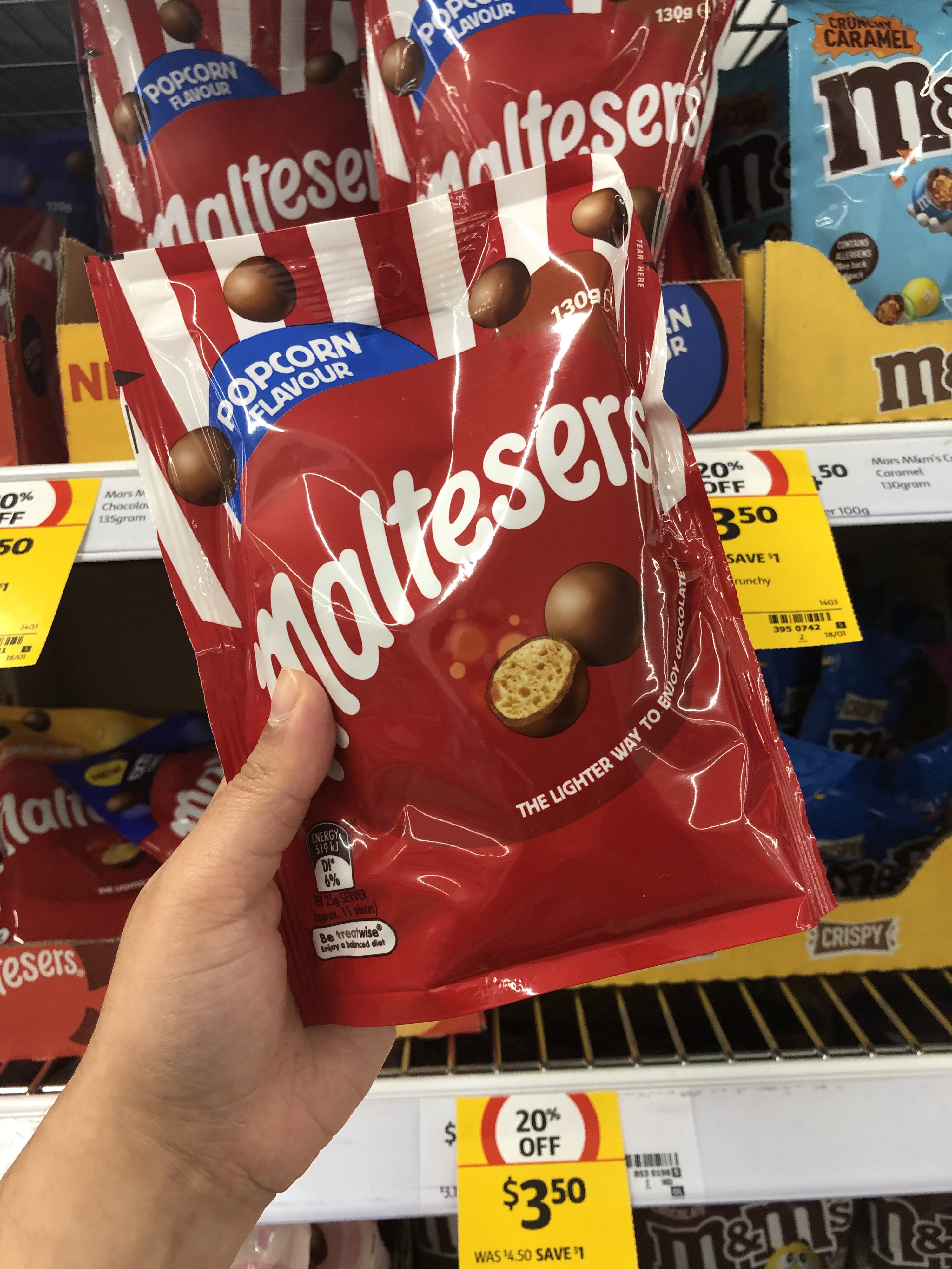 A hand holding a bag of popcorn flavour Maltesers in front of a grocery store shelf