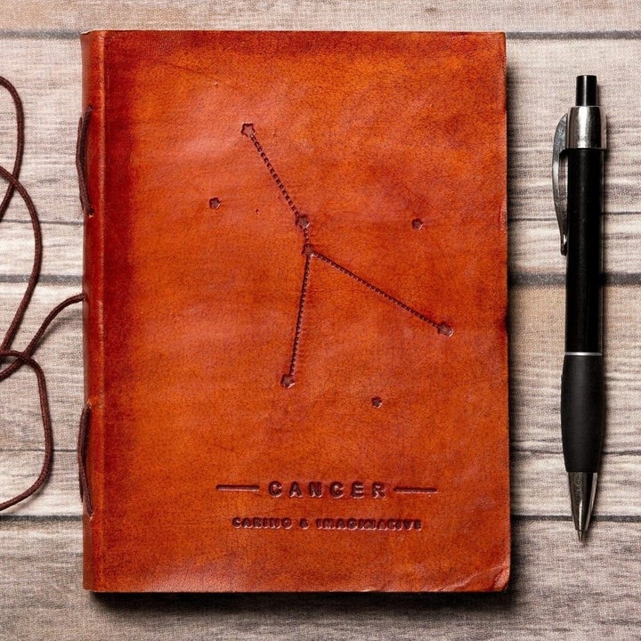 a brown leather journal embossed with the words "cancer, caring & imaginative" and a constellation