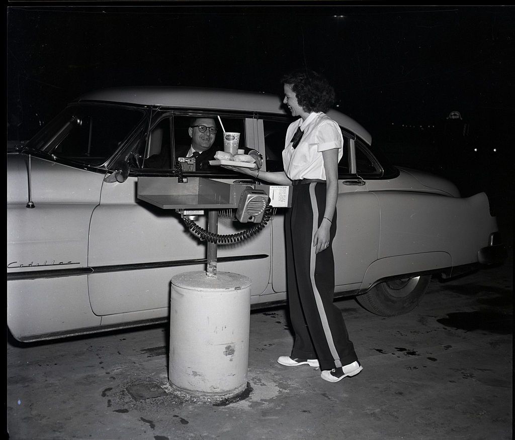 A carhop delivering food to a man at a drive-in restaurant