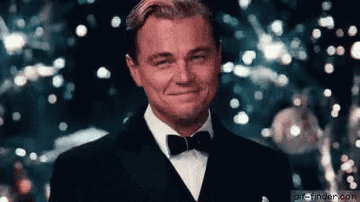 Leo's character in the Great Gatsby raising a glass in cheers as fireworks go off behind him