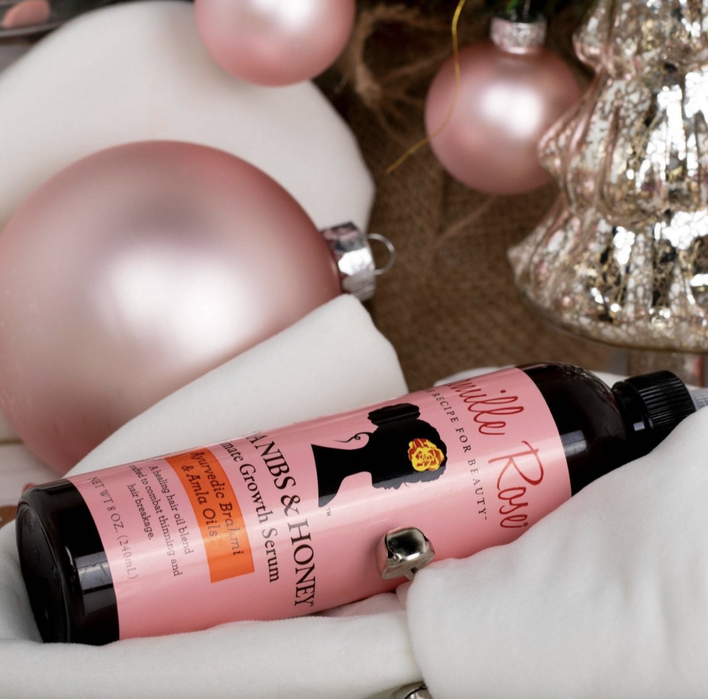 A bottle of hair growth serum with pink and white Christmas ornaments