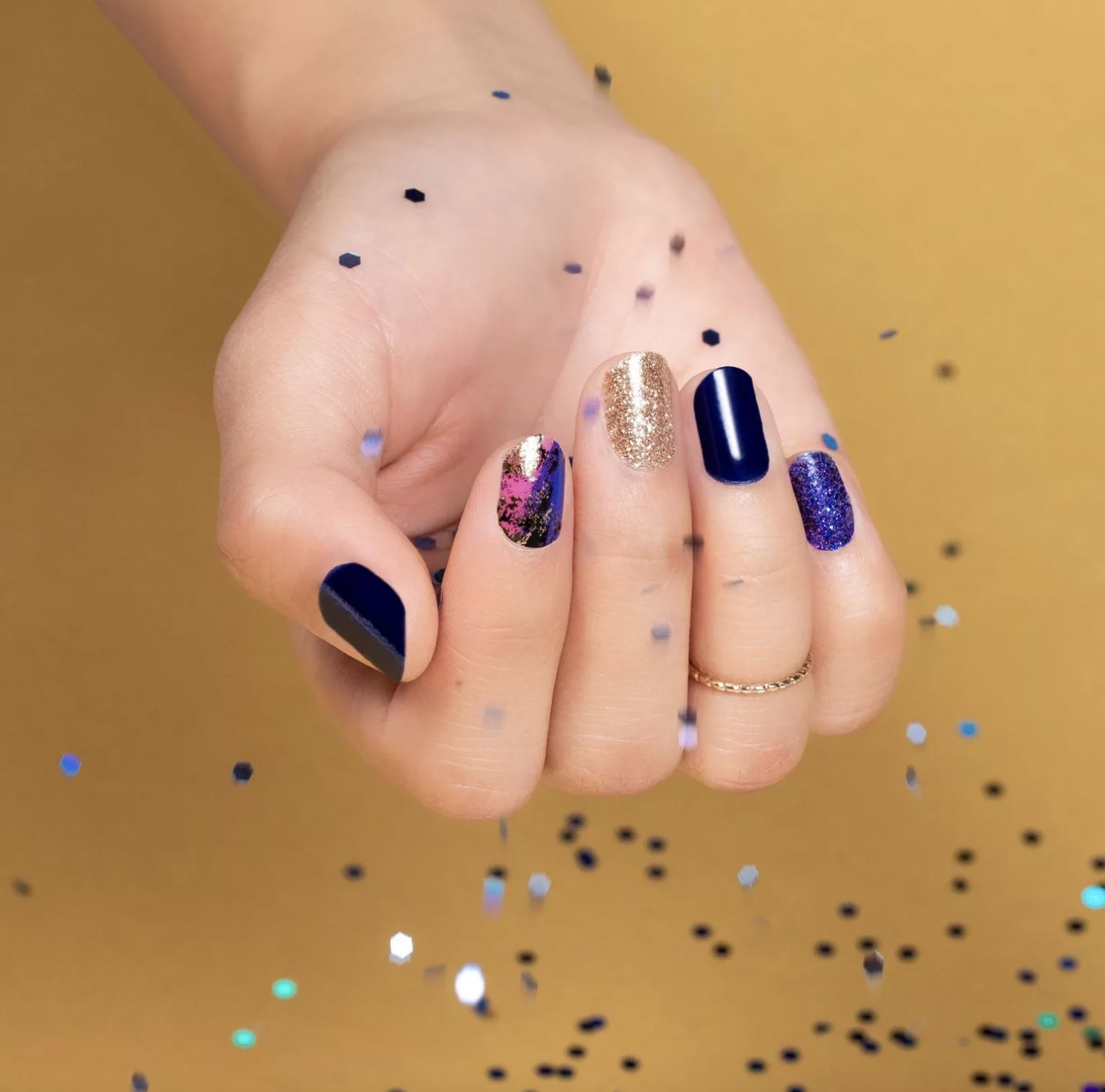 A person showing off a blue, sparkly manicure while holding silver confetti strips