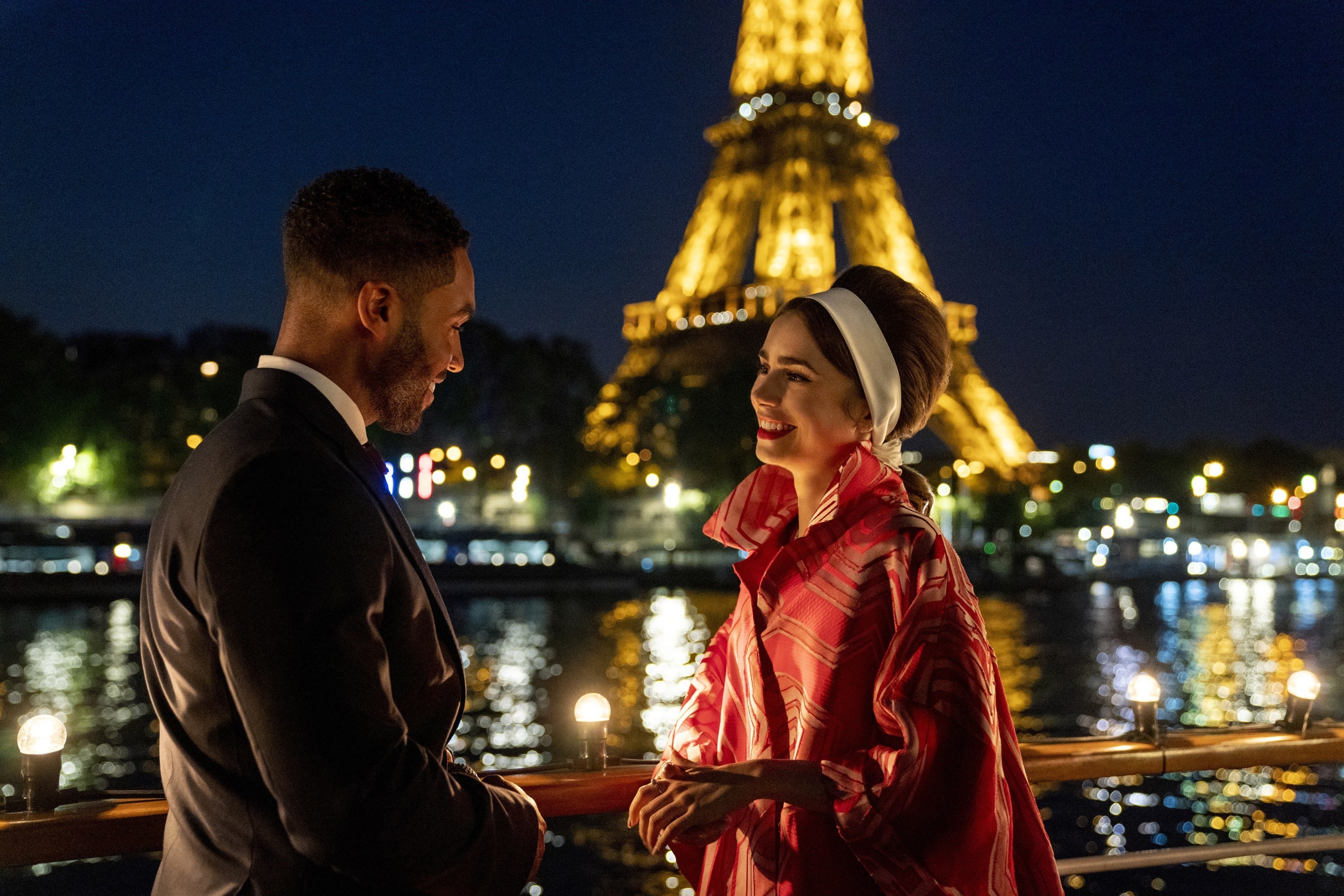 Still from &quot;Emily in Paris&quot; featuring Lucien Laviscount (L) and Lily (R) with the Eiffel Tower and the Seine River in the background at nighttime