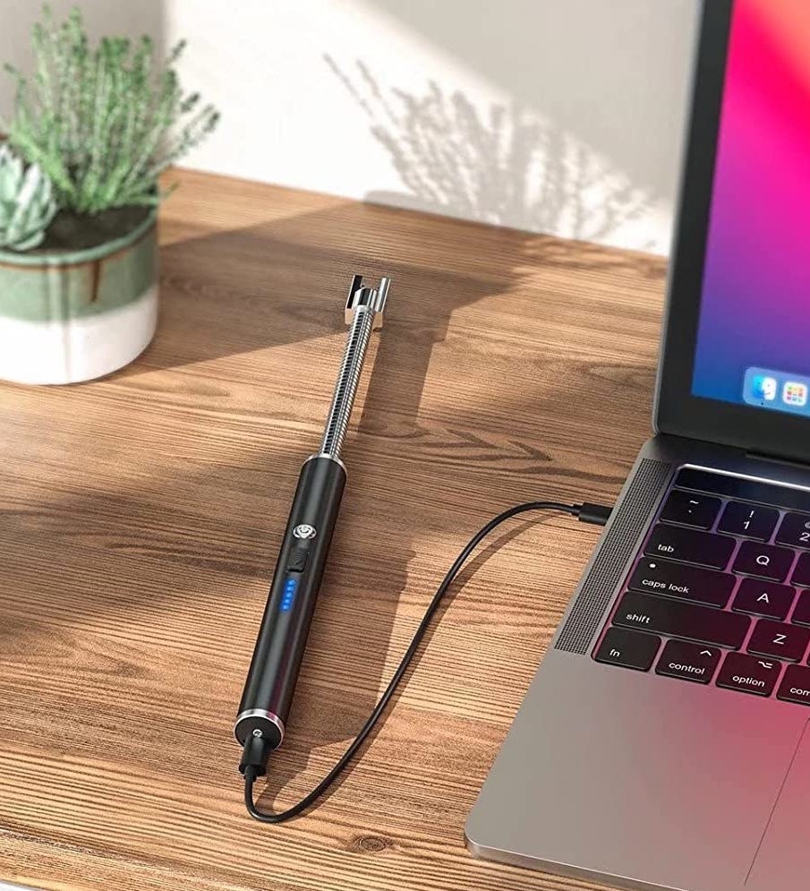 The lighter plugged into a laptop on a wooden table next to a plant