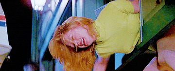 Girl stuck in a cat-flap in a garage door while it moves upwards. Her legs are kicking and she&#x27;s screaming. She&#x27;s wearing a yellow top and a patterned skirt.