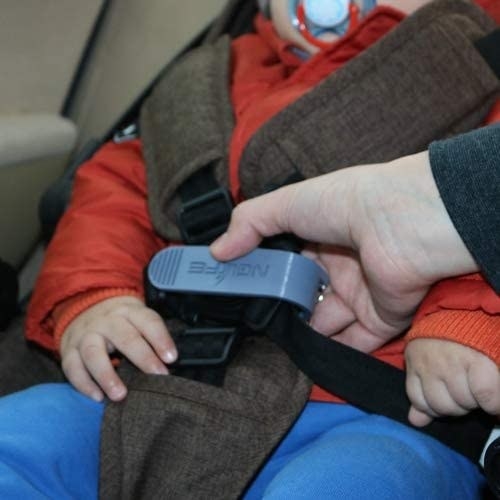 A person using a small squeeze tool to unbuckle their kid in a car seat