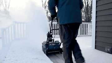 A person using the snow blower to clear their deck
