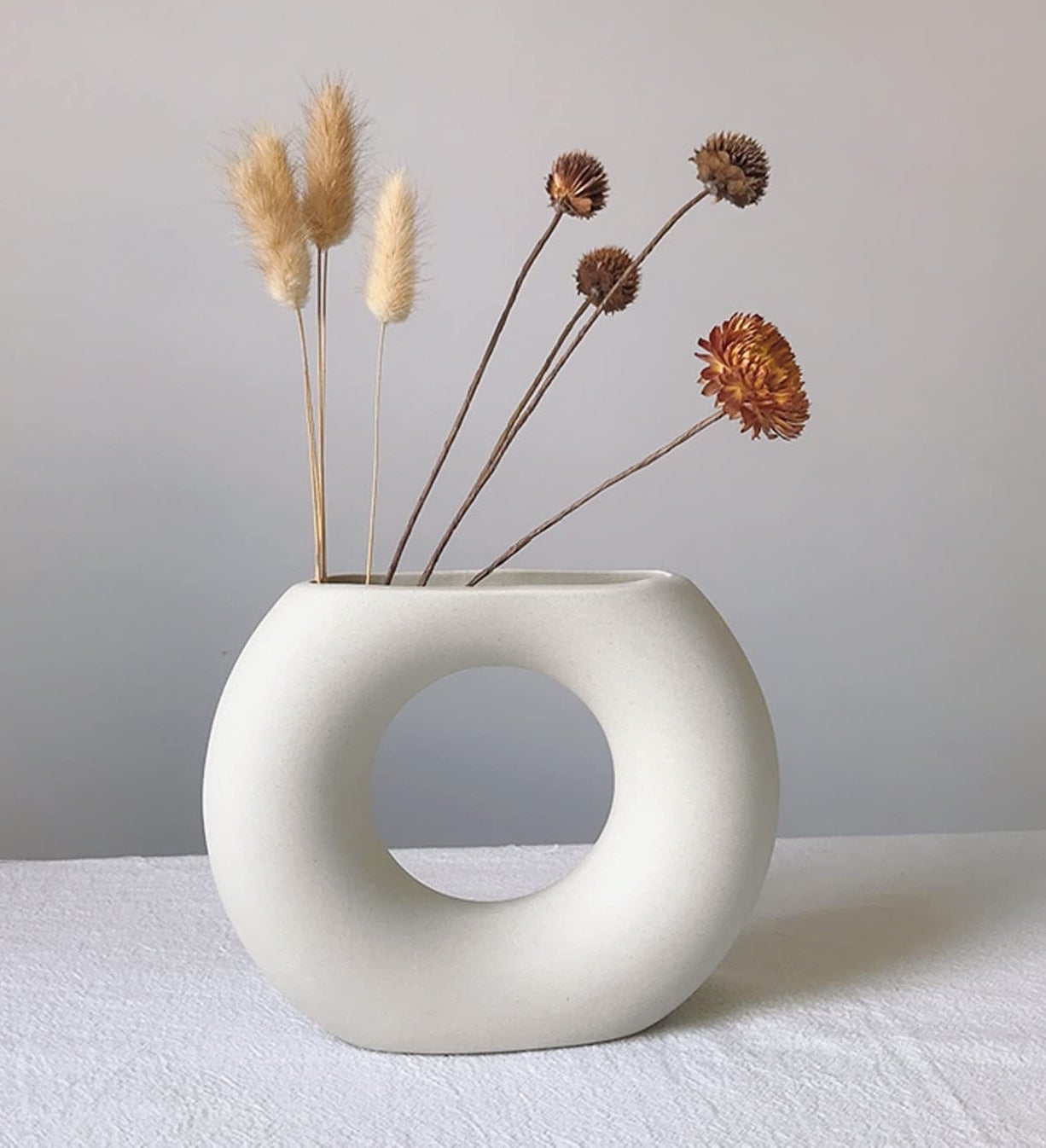 a matte ceramic vase in a circular shape filled with dried flowers