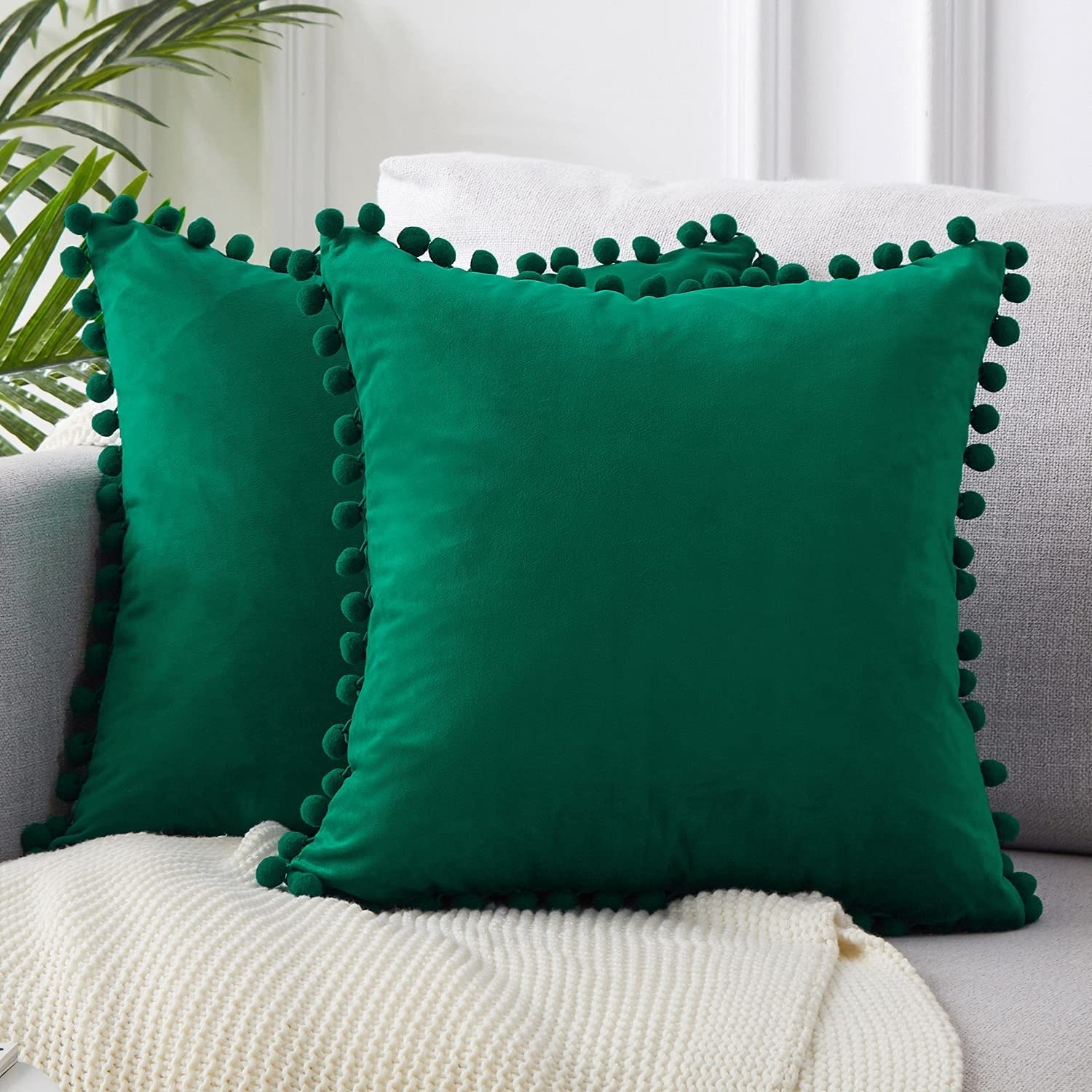 a pair of jewel-toned pillow shams with decorative pom poms around the edges